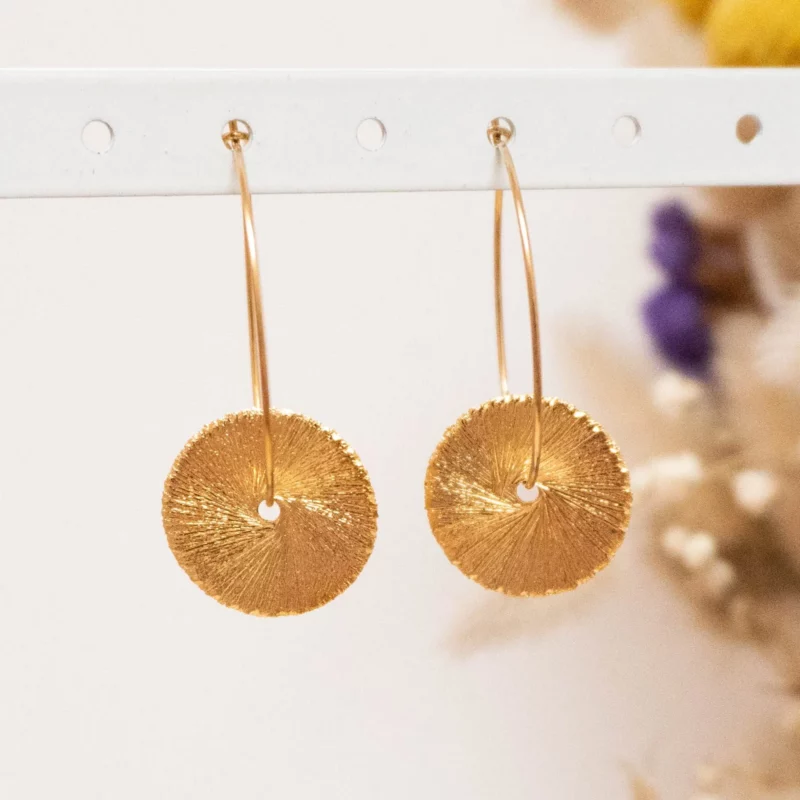 Créoles en acier inoxydable ornées de deux disques, pleins de détails en reliefs qui reflètent la lumière sur une attache ronde