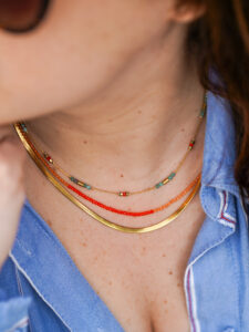 Collier ras de cou en acier inoxydable coloré composé d’une chaine serpentine et de petites perles en verre rouge et de pierres de turquoises
