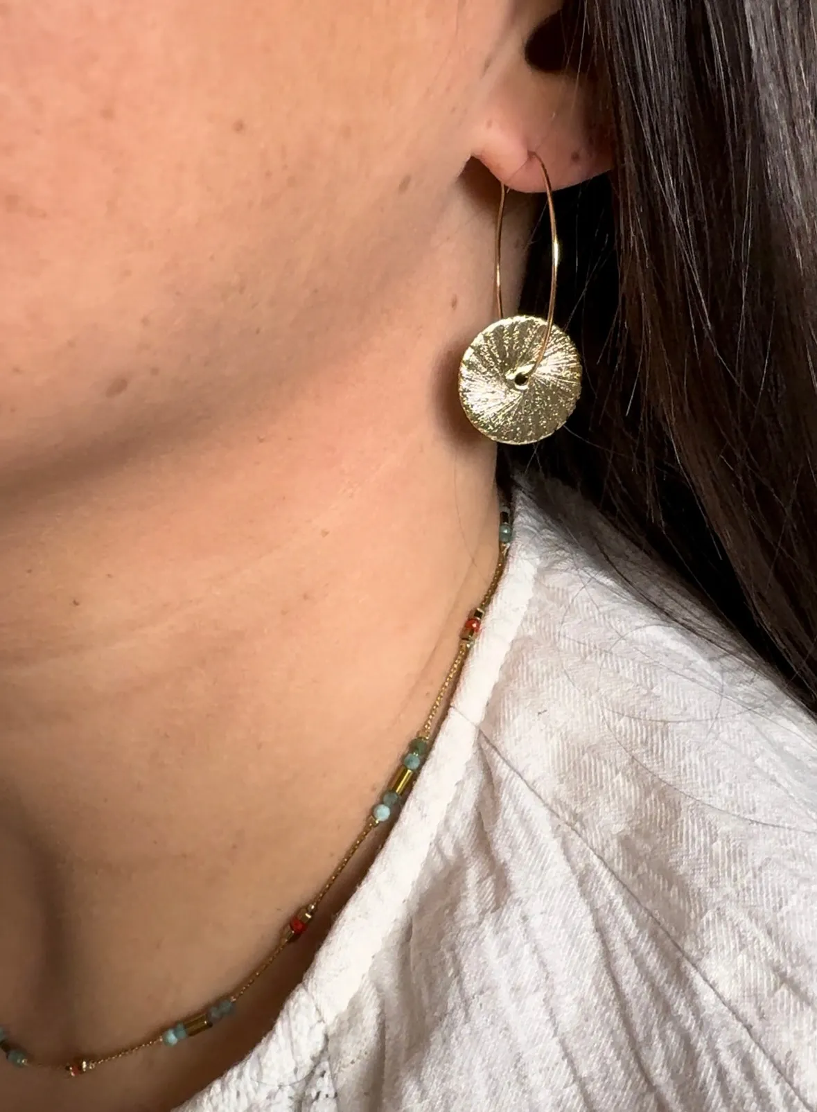 Créoles en acier inoxydable ornées de deux disques, pleins de détails en reliefs qui reflètent la lumière sur une attache ronde